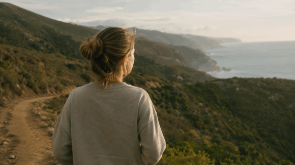 Eine Person steht von hinten auf einem Küstenpfad und blickt ruhig in die weite Landschaft. Das Bild vermittelt Selbstvertrauen, innere Stärke und einen hoffnungsvollen Blick nach vorn.